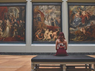 Woman sitting on a bench admiring large paintings in a museum