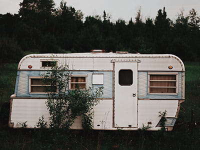 white RV trailer on grass field near trees under cloudy sky