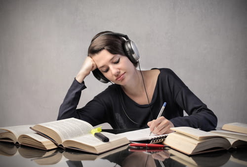 student with headphones studying around a table full of books