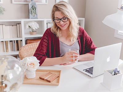 woman smiling holding glass mug sitting beside table with MacBook